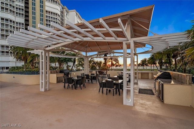 patio terrace at dusk with a bar, an outdoor kitchen, and a pergola