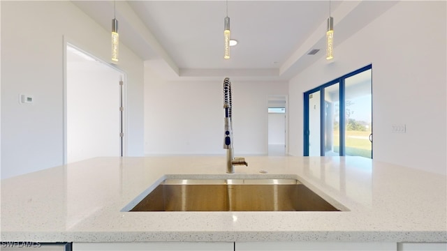 details featuring a tray ceiling, light stone counters, sink, and pendant lighting