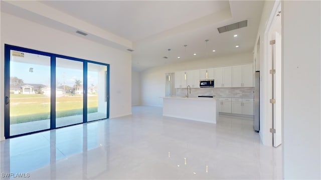 kitchen featuring tasteful backsplash, sink, hanging light fixtures, white cabinetry, and a center island with sink