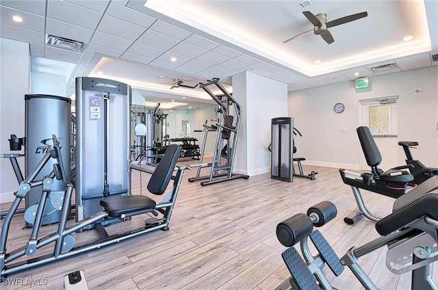 workout area featuring light hardwood / wood-style flooring, a raised ceiling, and ceiling fan