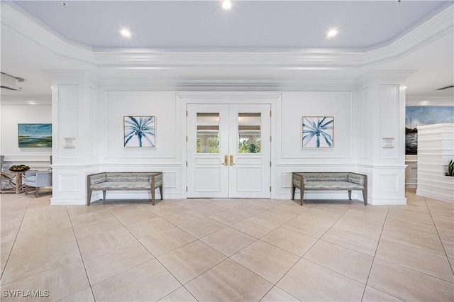 foyer featuring crown molding, light tile patterned flooring, a decorative wall, and a tray ceiling