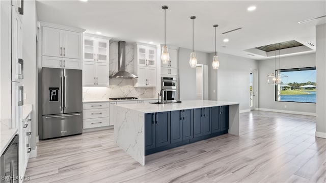 kitchen with wall chimney exhaust hood, white cabinetry, stainless steel appliances, and a center island with sink