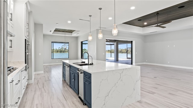 kitchen featuring sink, pendant lighting, white cabinets, blue cabinetry, and a kitchen island with sink