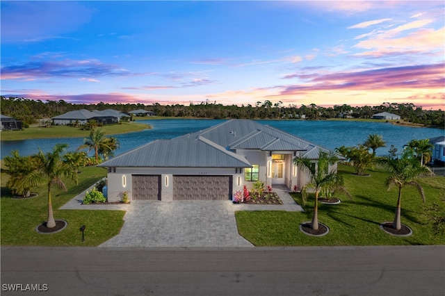 view of front facade with a garage, a yard, and a water view