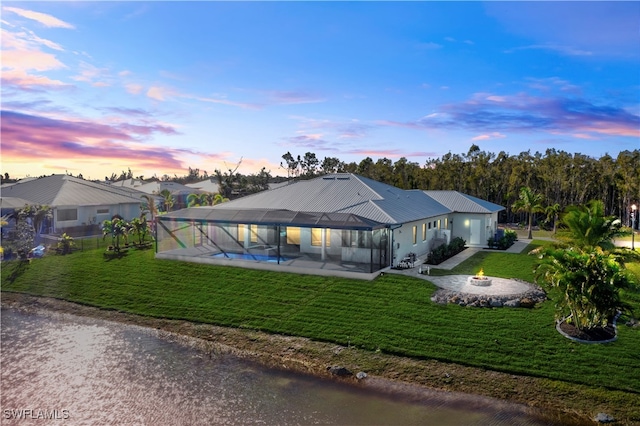 back house at dusk with a pool, a patio, and a lawn