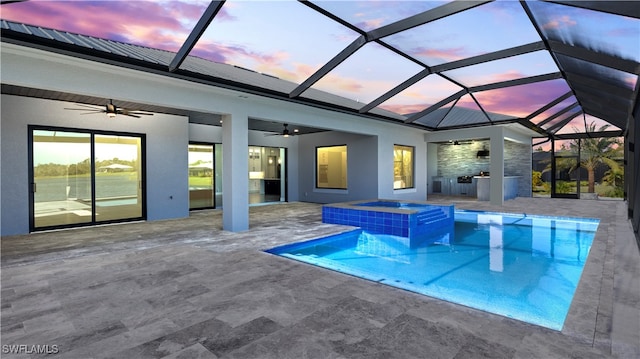 pool at dusk with an in ground hot tub, a patio, glass enclosure, and ceiling fan