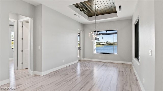 spare room featuring light hardwood / wood-style floors, a notable chandelier, and a tray ceiling