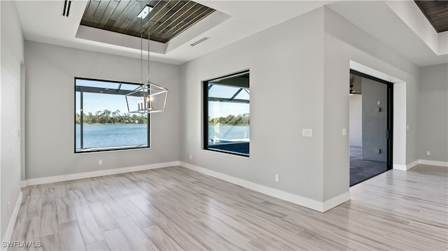 empty room with a wealth of natural light, a chandelier, light hardwood / wood-style flooring, and a tray ceiling