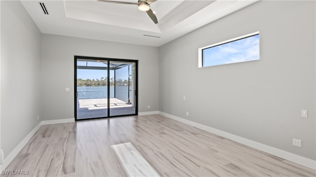 spare room with light hardwood / wood-style flooring, a healthy amount of sunlight, a tray ceiling, and a water view