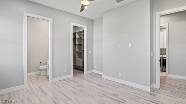 unfurnished bedroom with a spacious closet, ensuite bath, light hardwood / wood-style flooring, and ceiling fan