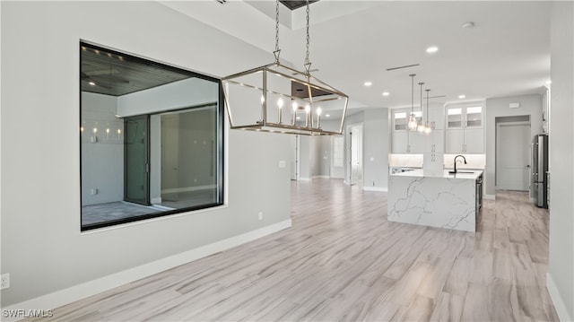 kitchen with white cabinets, high end refrigerator, light wood-type flooring, pendant lighting, and sink