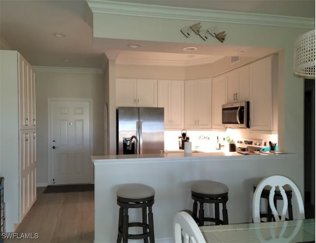 kitchen featuring white cabinetry, crown molding, stainless steel appliances, and hardwood / wood-style floors