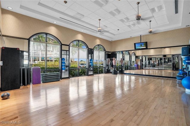 gym with ceiling fan, a raised ceiling, a high ceiling, and wood finished floors