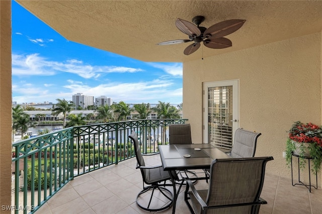 balcony with a city view, outdoor dining area, a ceiling fan, and a water view