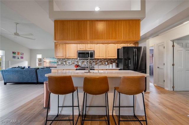 kitchen featuring ceiling fan, stainless steel appliances, vaulted ceiling, light hardwood / wood-style flooring, and light brown cabinets