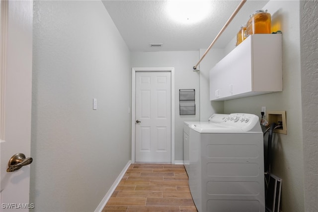 laundry area with light hardwood / wood-style flooring, washer and dryer, a textured ceiling, and cabinets