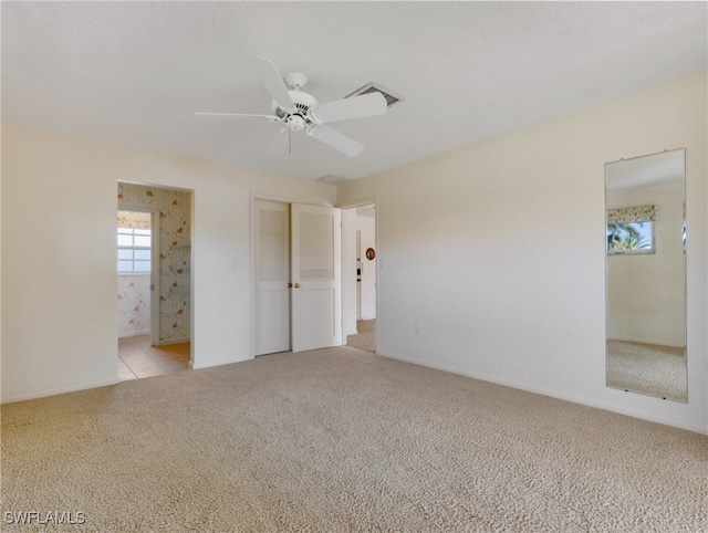 unfurnished bedroom featuring connected bathroom, light colored carpet, and ceiling fan