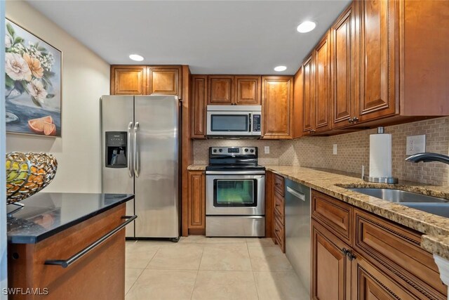 380 Seaview Ct Unit 1808, Marco Island, FL 34145 - kitchen featuring stainless steel appliances, a sink, brown cabinetry, light tile patterned flooring, and stone countertops