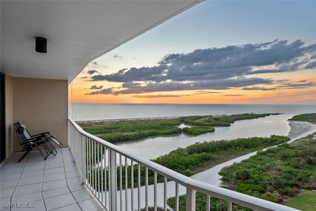 balcony at dusk featuring a water view