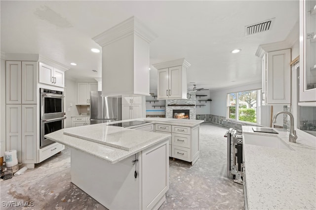 kitchen featuring a kitchen island, appliances with stainless steel finishes, white cabinetry, a stone fireplace, and light stone counters