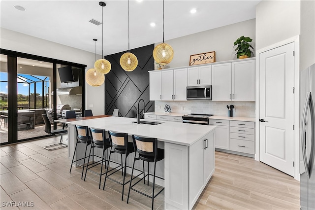 kitchen with decorative light fixtures, sink, stainless steel appliances, and an island with sink