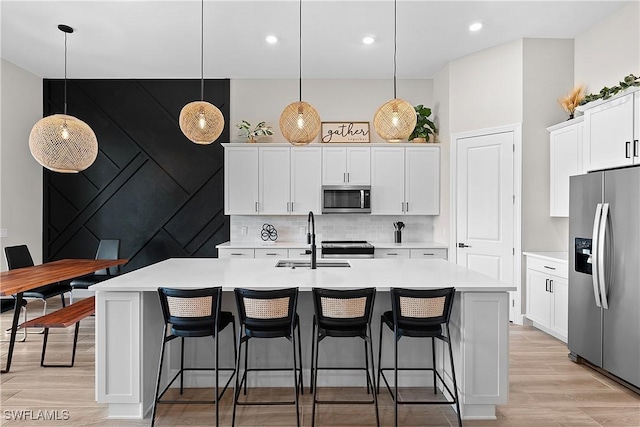 kitchen featuring a kitchen island with sink, stainless steel appliances, and decorative light fixtures