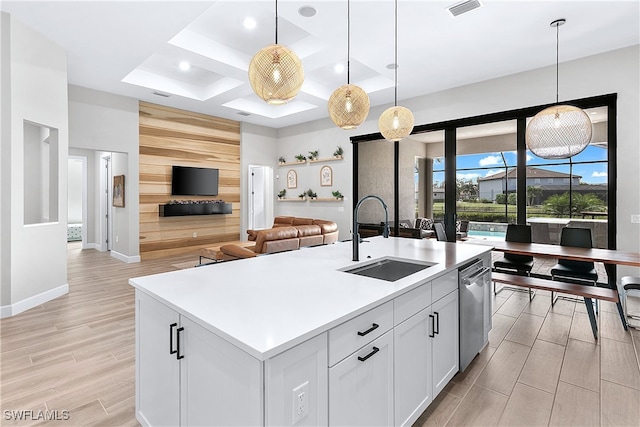 kitchen featuring a kitchen island with sink, white cabinets, hanging light fixtures, sink, and stainless steel dishwasher