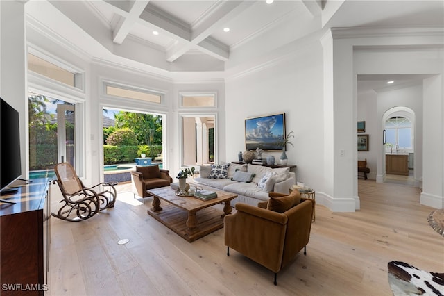 living room with beam ceiling, a high ceiling, coffered ceiling, light hardwood / wood-style flooring, and ornamental molding