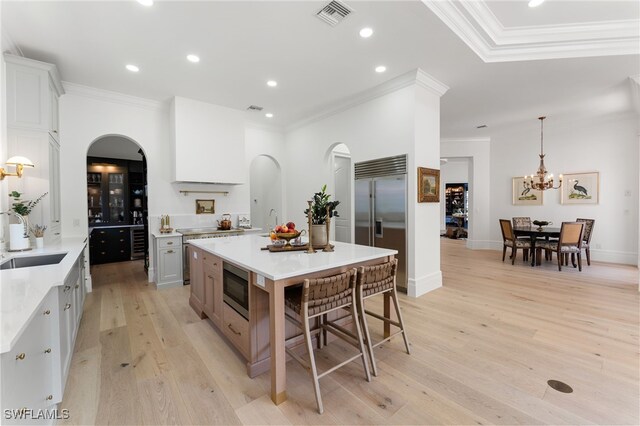 kitchen with a spacious island, built in appliances, decorative light fixtures, white cabinets, and light hardwood / wood-style floors