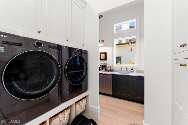 washroom featuring cabinets, sink, light hardwood / wood-style floors, and washing machine and clothes dryer