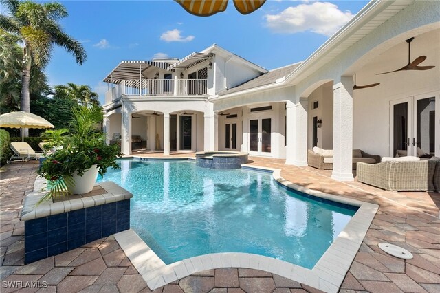 back of property with french doors, ceiling fan, a swimming pool with hot tub, a balcony, and a patio area