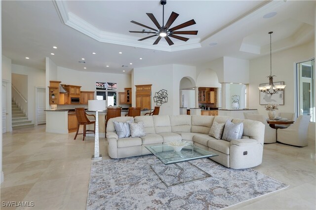 living room featuring a tray ceiling, ceiling fan with notable chandelier, and ornamental molding