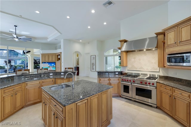 kitchen with sink, wall chimney range hood, stainless steel appliances, and an island with sink