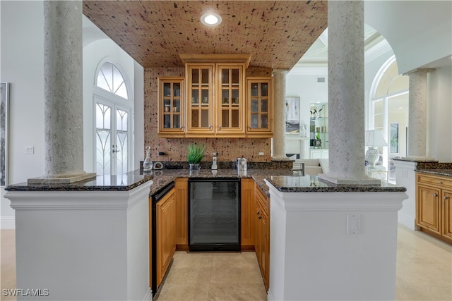 kitchen featuring kitchen peninsula, dark stone countertops, ornate columns, and wine cooler