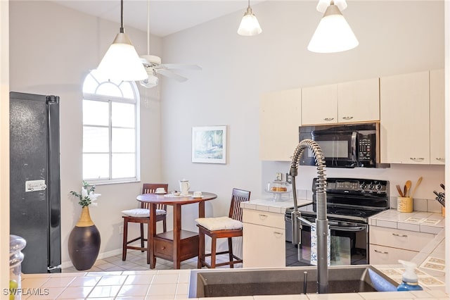 kitchen featuring tile countertops, black appliances, light tile patterned floors, and pendant lighting