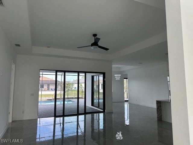 empty room with ceiling fan and a raised ceiling