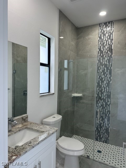 bathroom featuring a shower with door, vanity, and toilet