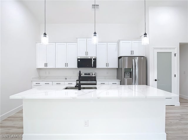 kitchen featuring appliances with stainless steel finishes, white cabinetry, hanging light fixtures, and an island with sink