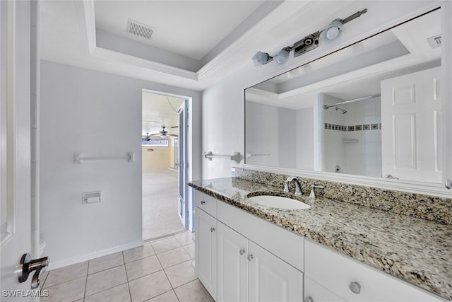 bathroom with ceiling fan, a tile shower, a tray ceiling, vanity, and tile patterned flooring