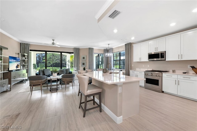 kitchen with appliances with stainless steel finishes, hanging light fixtures, a kitchen island with sink, and white cabinetry