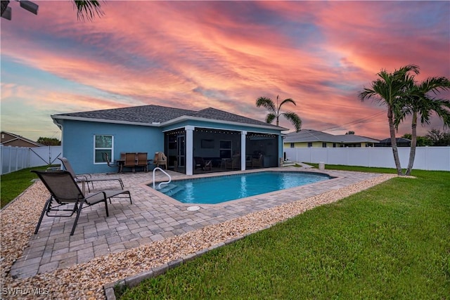 pool at dusk featuring a lawn, a sunroom, and a patio