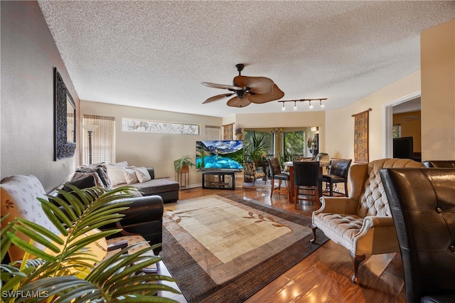 living room featuring a textured ceiling, rail lighting, wood-type flooring, and ceiling fan