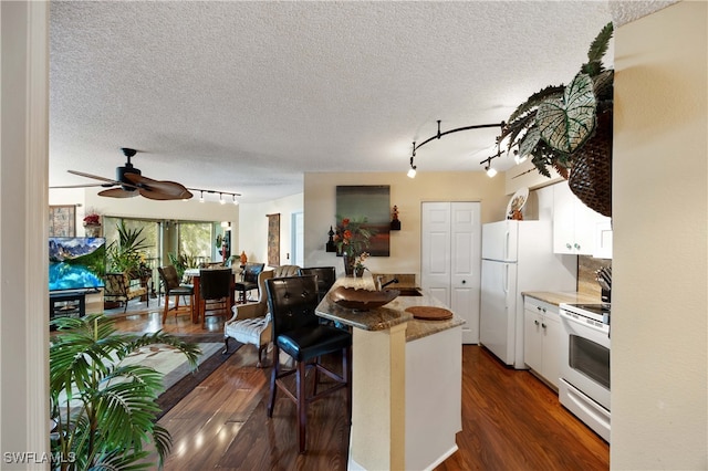 kitchen featuring dark hardwood / wood-style flooring, a kitchen breakfast bar, white cabinetry, a textured ceiling, and white appliances