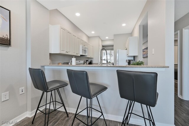 kitchen with dark hardwood / wood-style flooring, kitchen peninsula, white appliances, a breakfast bar, and white cabinets