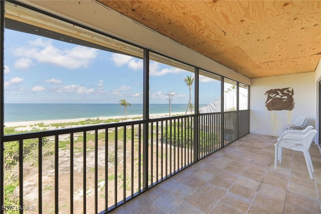 unfurnished sunroom with wood ceiling, a water view, and a beach view