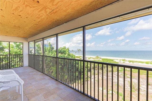 unfurnished sunroom featuring a water view, wood ceiling, and a beach view