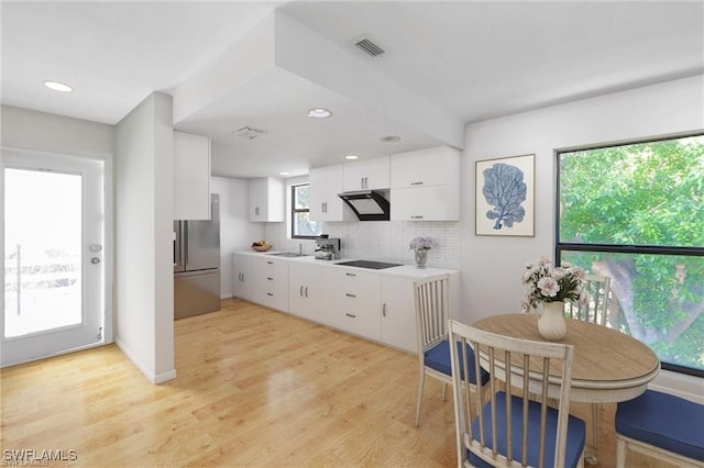 kitchen featuring decorative backsplash, white cabinetry, stainless steel refrigerator, light hardwood / wood-style flooring, and black electric stovetop