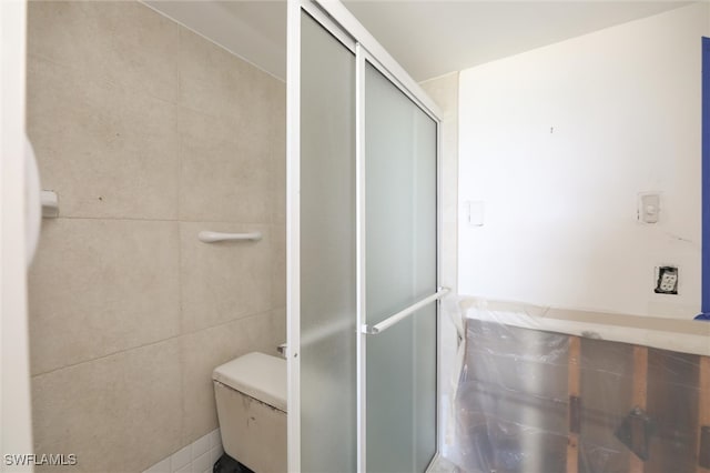 bathroom featuring toilet, tile walls, and an enclosed shower