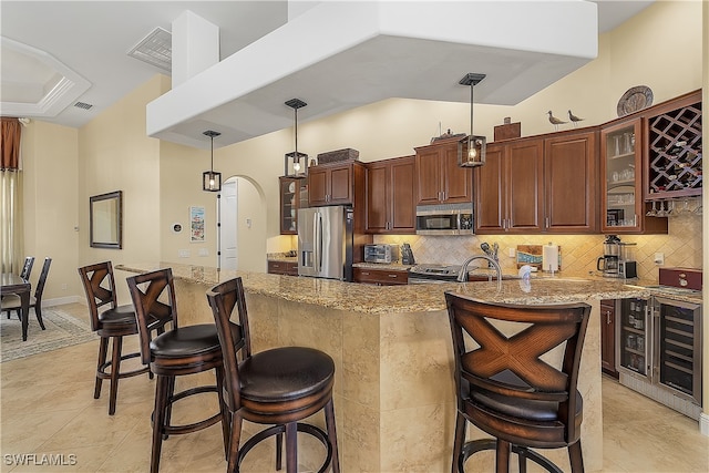 kitchen with tasteful backsplash, hanging light fixtures, an island with sink, appliances with stainless steel finishes, and a kitchen breakfast bar