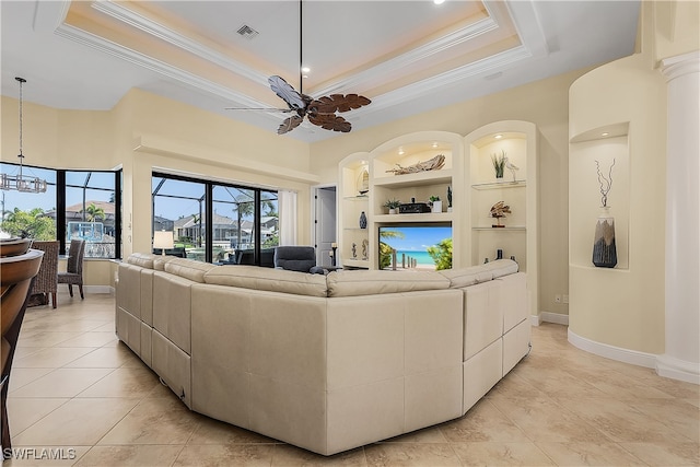 living room featuring ornamental molding, light tile patterned floors, a raised ceiling, built in shelves, and ceiling fan with notable chandelier